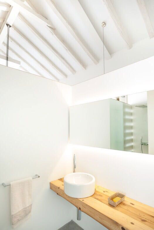 Interior baño abuhardillado. Acabados blancos con repisa de madera.