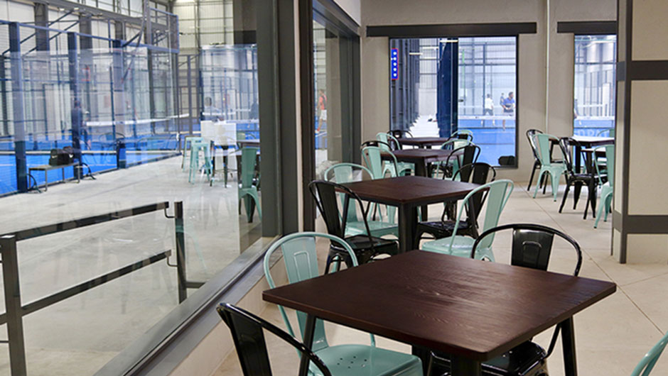 Vista interior de salón de bar junto pistas de padel construidas en una antigua nave industrial