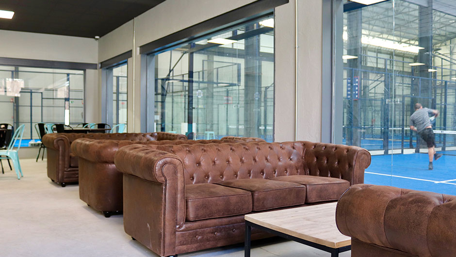 Vista interior de salón de bar junto pistas de padel construidas en una antigua nave industrial