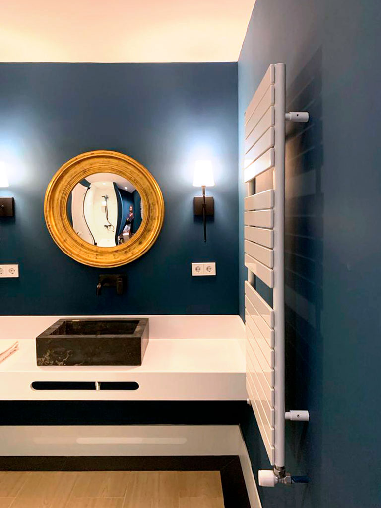 Vista baño con paredes azul marino y espejo circular dorado.