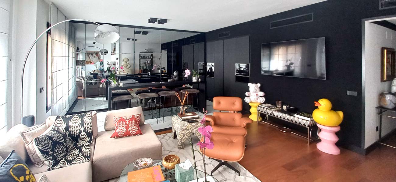 Interior vivienda con un gran panel trasero de espejo. Suelo de madera y pared negra contrastando con el gran ventanal opuesto.