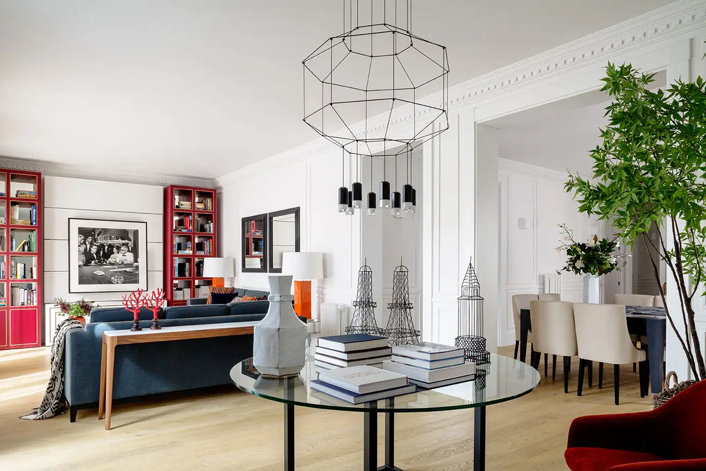 Vista interior del salón de una vivienda con paredes blancas y suelo de madera. Decoración minimalista con toque de color rojo en la estantería.