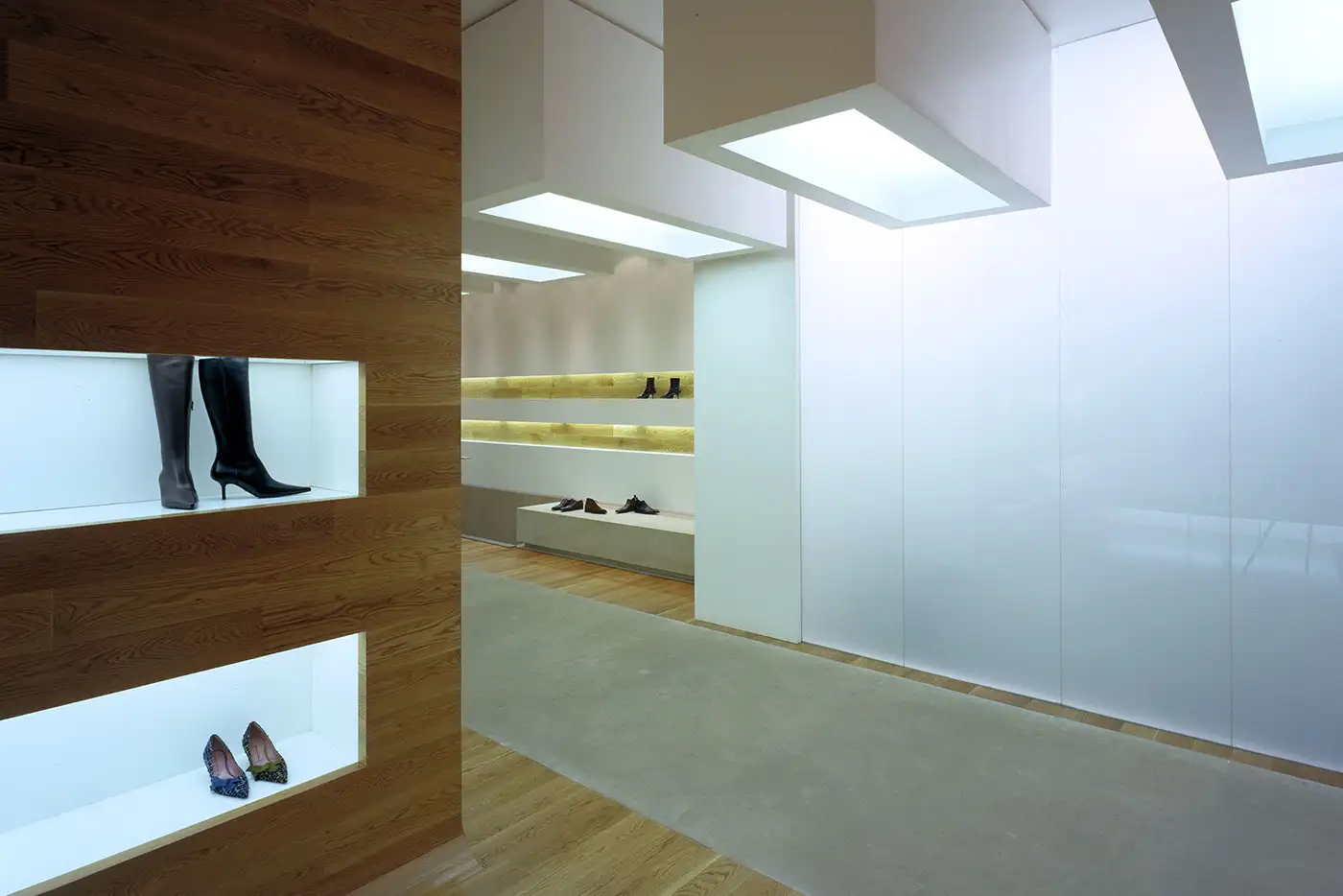 Vista lateral del panel frontal con estánterías encastradas. Interior zapatería, decoración minimalista, suelo de madera. Tonos crema suave.