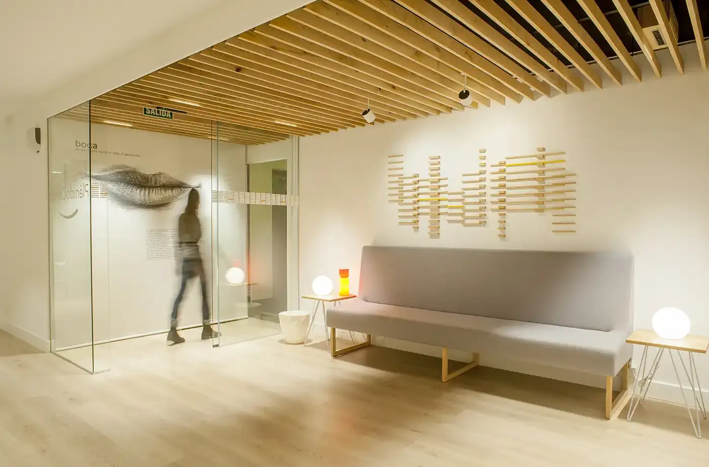 Interior clínica dental. Vista sala de espera. Iluminación cálida, tonos crema y madera.