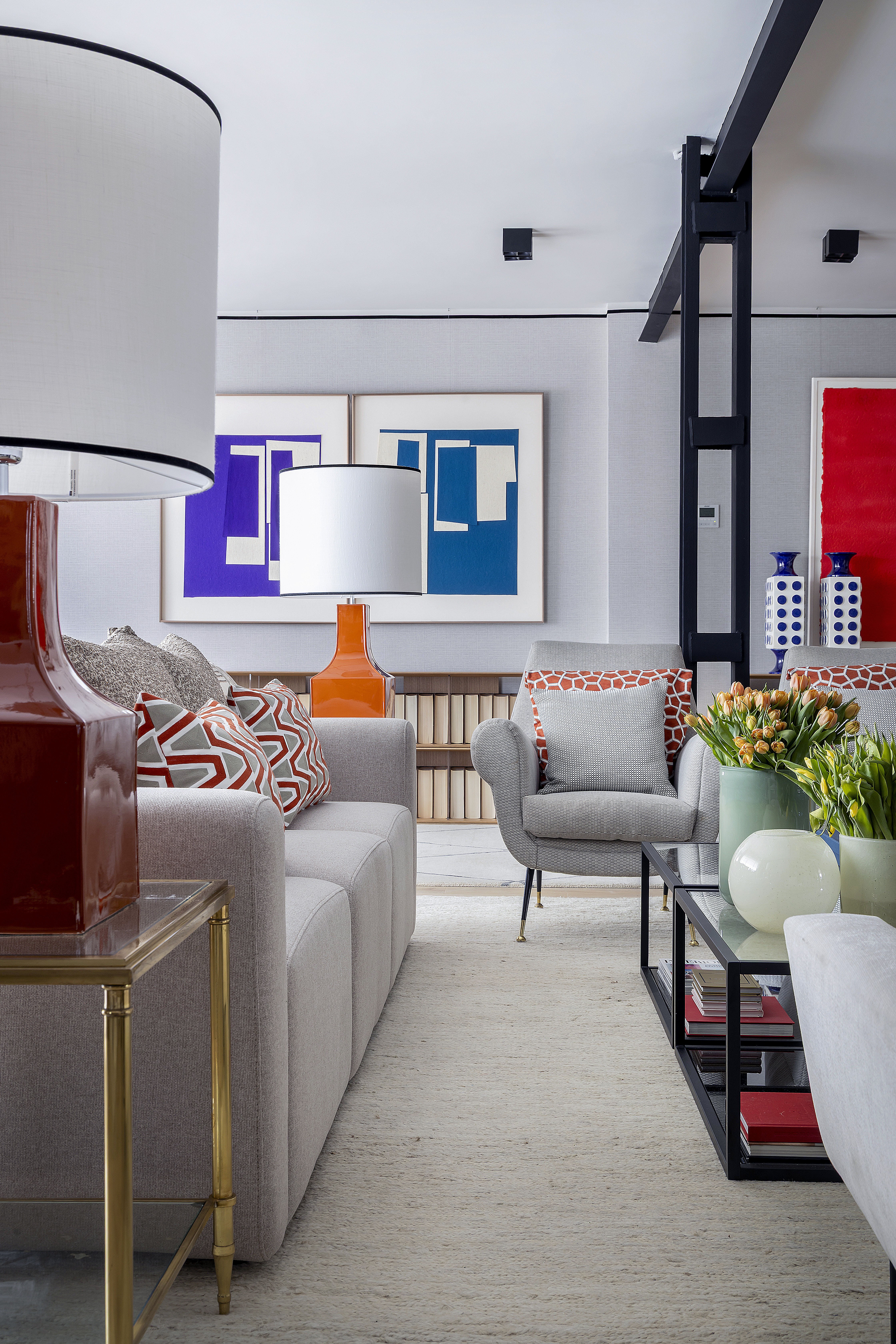 Vista frontal del salón con sofá, butaca, mesas auxiliares, lámparas decorativas y obras de arte en la pared.