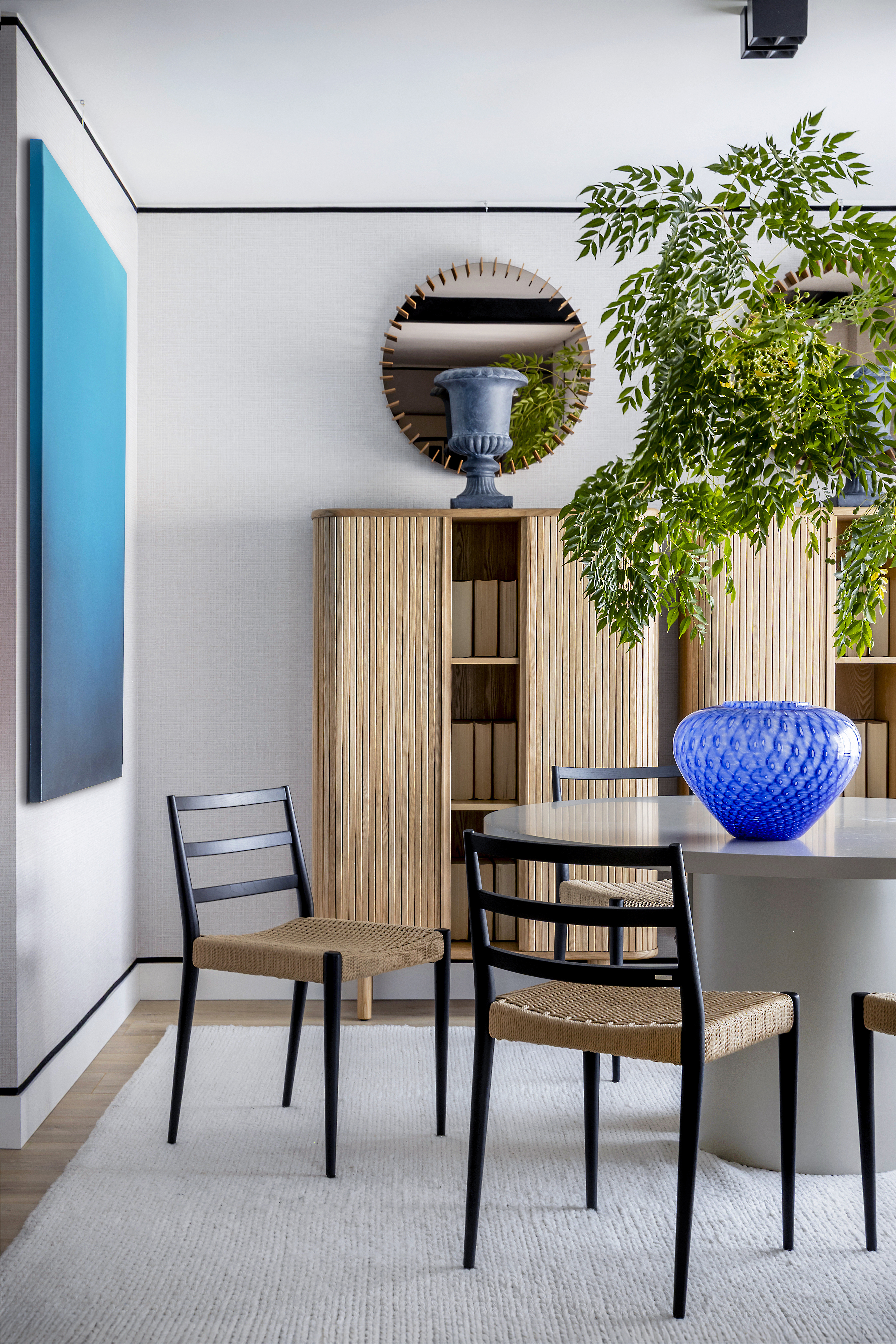 Detalle del comedor con mesa y sillas, mueble de almacenaje, elementos decorativos y planta.