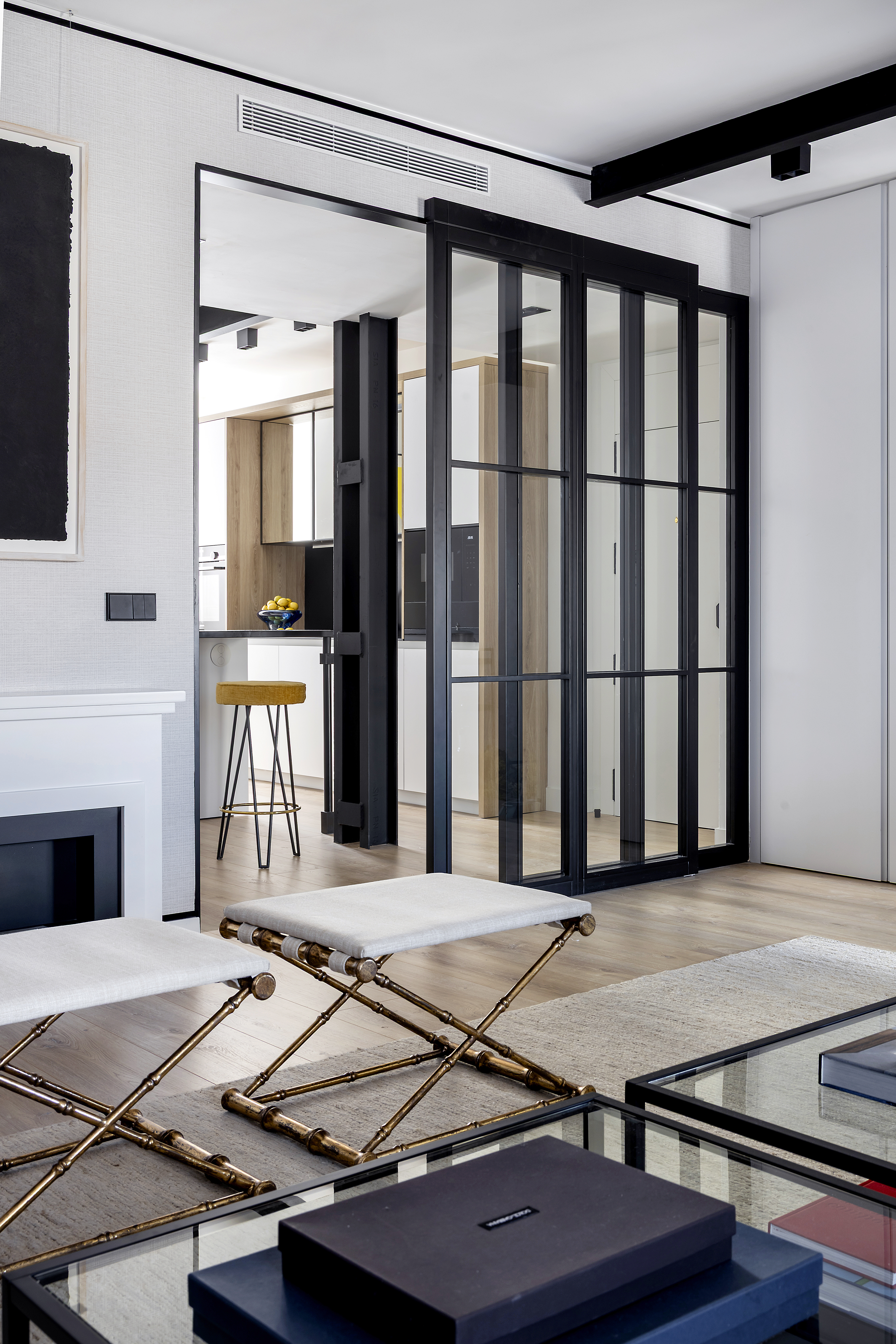 Conexión entre el salón y la cocina mediante puerta corredera acristalada, con mobiliario auxiliar en primer plano.