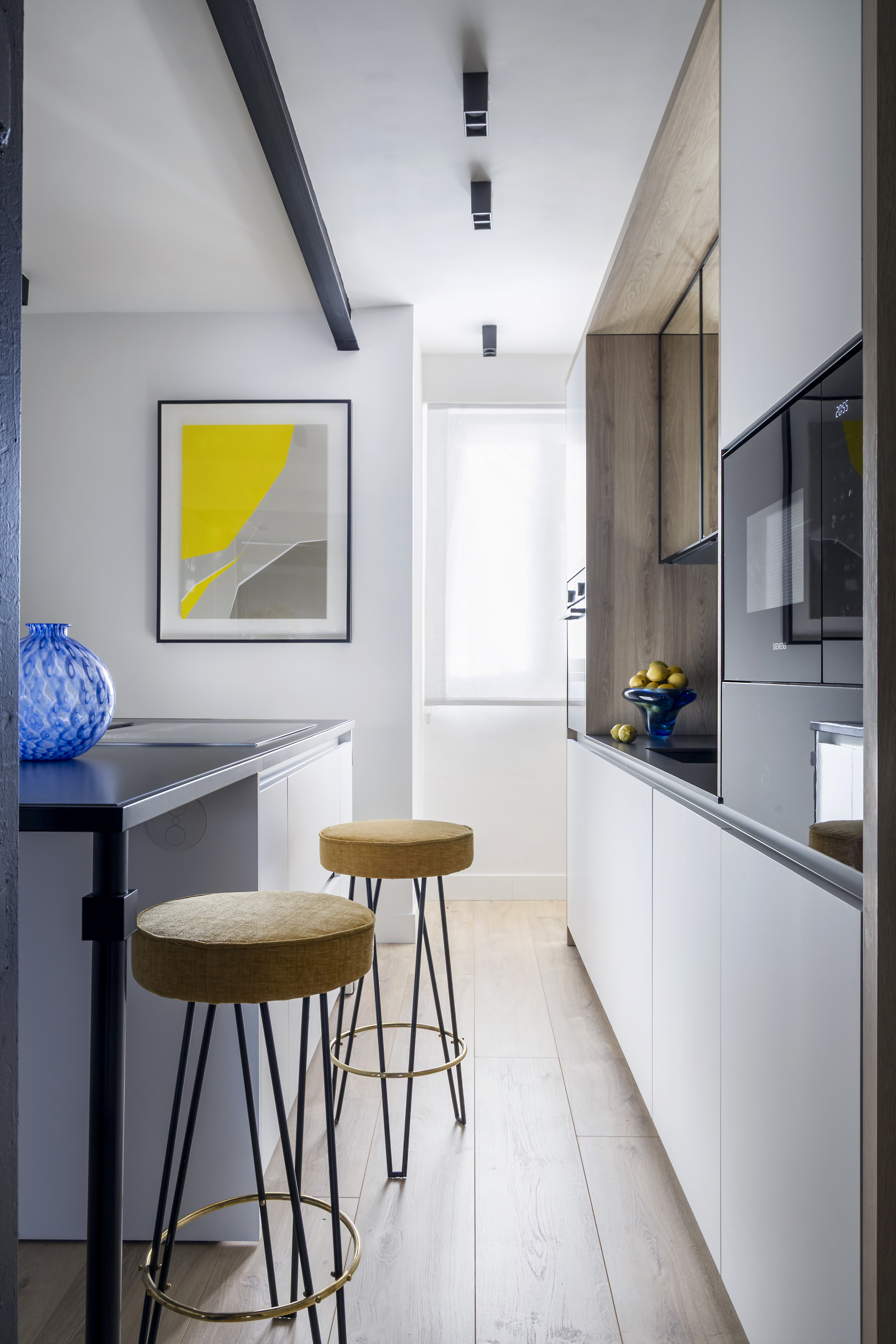 Vista interior de la cocina con distribución lineal, barra con taburetes, mobiliario integrado y electrodomésticos.