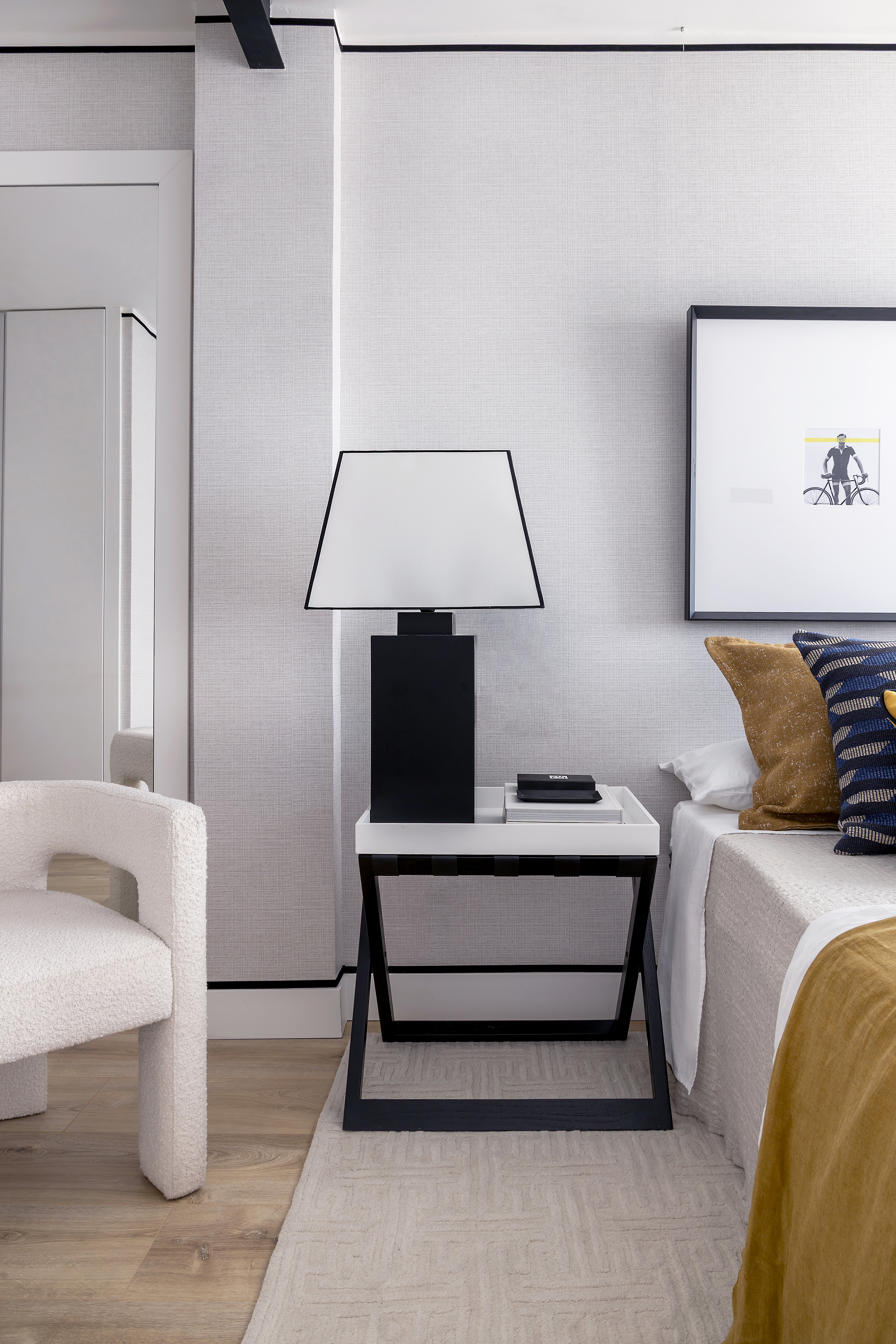 Detalle del dormitorio con mesilla de noche, lámpara de sobremesa, cama vestida y sillón auxiliar.